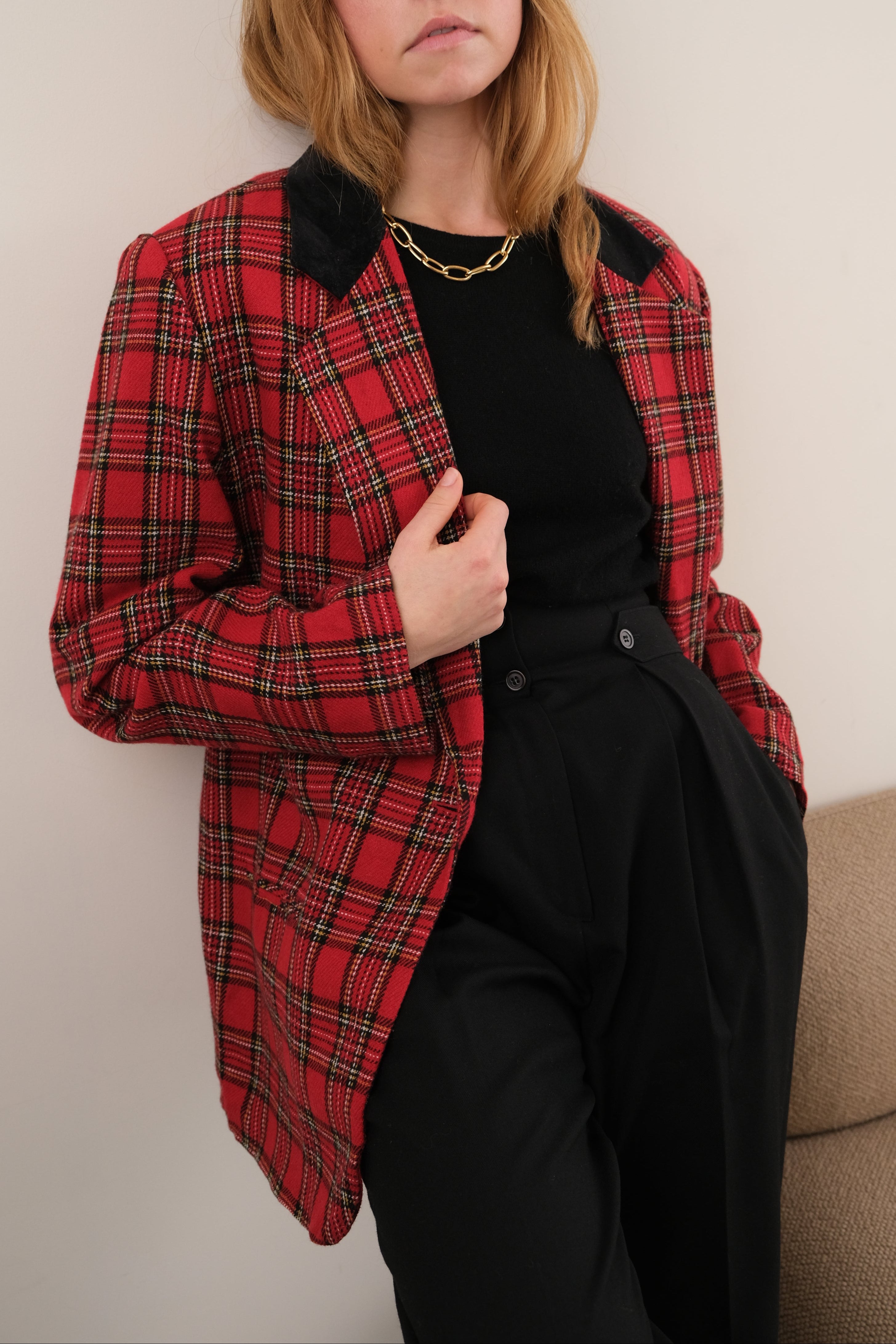 Person wearing a red plaid jacket over a black outfit on a neutral background