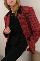 Person wearing a red plaid coat over a black outfit on a plain background